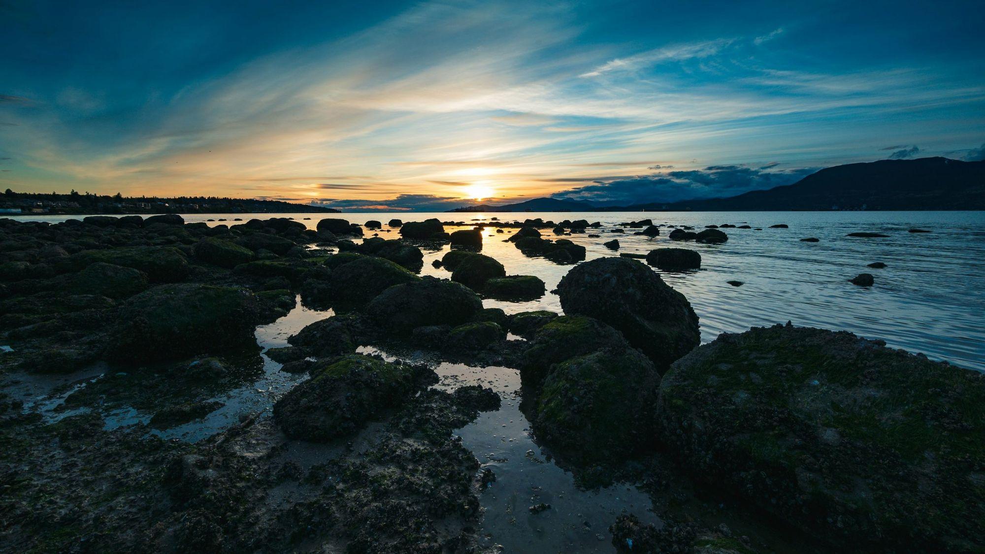 Rocky shoreline and calm water at Kitsilano Beach at sunset